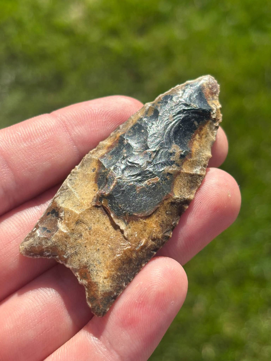 Angled view of the River Candy Clovis showing the dark central flute, golden-brown edges, and tip.
